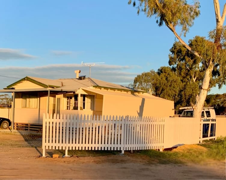 Our cottage in golden sunset light. The building is painted a creamy white, and there is a white picket fence out the front.