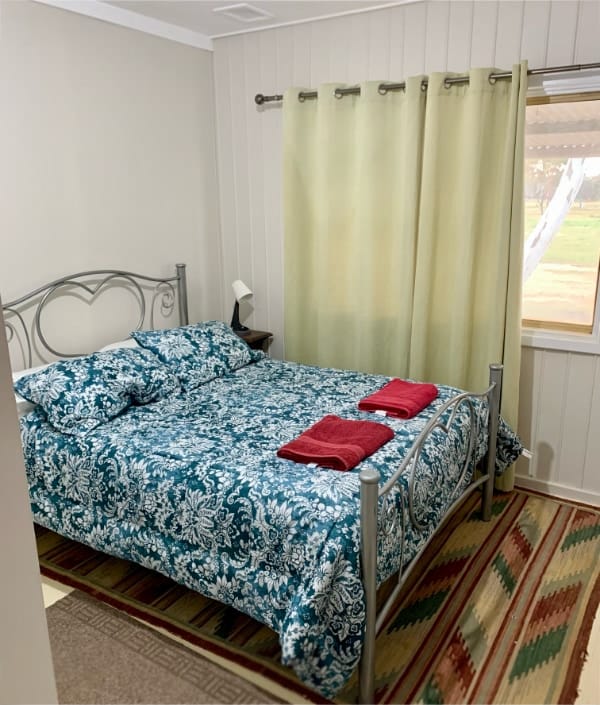 A double bed made up with a floral design quilt in the master bedroom. There is a view of eucalyptus trees outside the window.