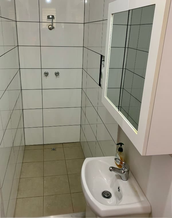 The refurbished bathroom, with a shower, toilet, wash basin, and mirror.
